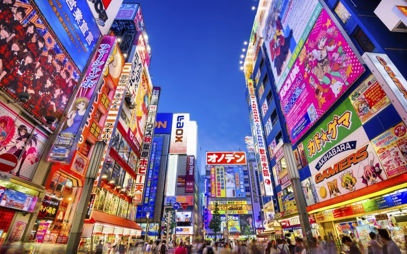 Tokyo, Japan - August 1, 2015: Crowds pass below colorful signs in Akihabara. The well known electronics district specializes in the sales of video games, anime, manga, and computer goods.